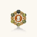 Ornate gold-plated brooch with central cameo, radiating spokes, pearl border, and green marbled natural stones on white background.